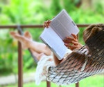 Woman reading a book on wooden decking in a UK garden