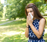 A woman sneezes in the park because of hay fever/allergies