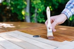 A person applies wood stain to a garden table.