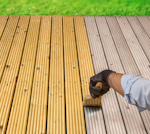 A gloved hand applies Roxil Enhanced Decking Oil with a brush.